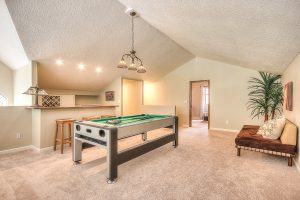 Interior photo of a carpeted leisure room with a pool table, a love seat, and a custom full sized bar.