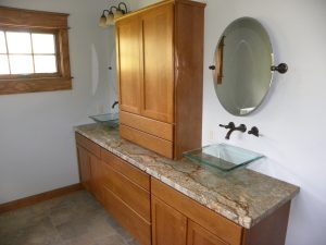 Custom design bathroom with granite countertops, wooden cabinets, glass sinks, and oval mirrors.