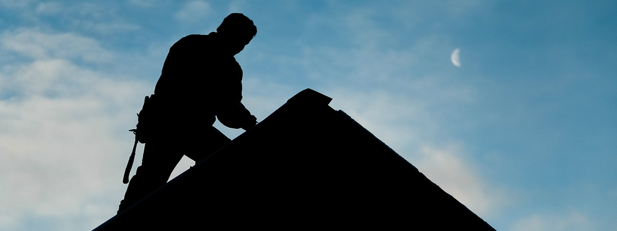 Silhouette of Man Working On Roof Peak