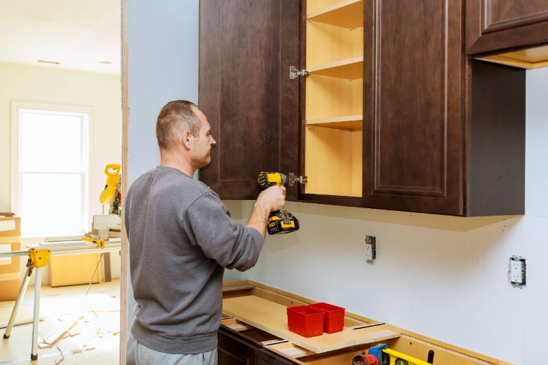 A worker installing brand new cabinets with natural wood tones.