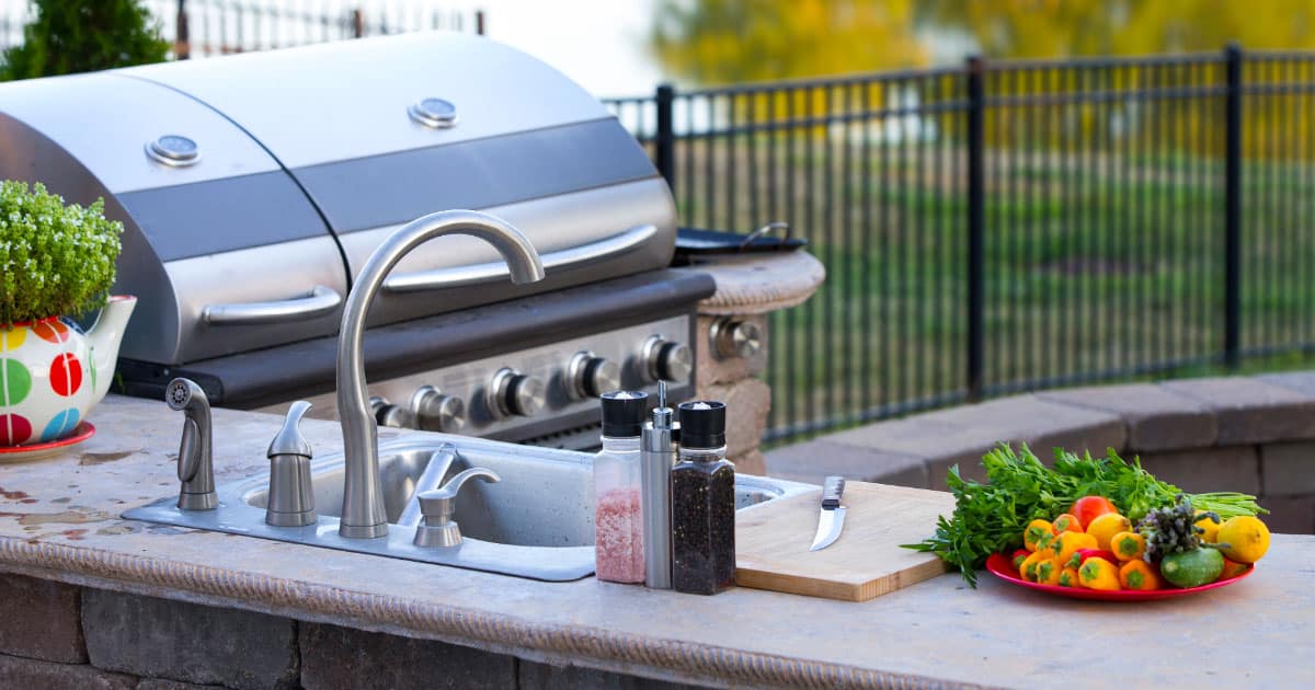 Outdoor kitchen with stainless steel grill, stone countertops, and sink